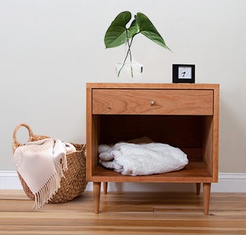 A wooden nightstand with a basket and a plant.