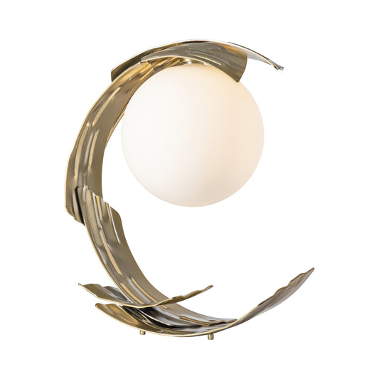 Hubbardton Forge Crest Table Lamp featuring a white globe light encircled by a wavy, gold spiral of hand-forged steel on a sleek white base.