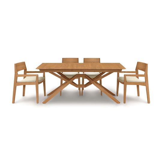 Exeter Extension Dining Table by Copeland Furniture with a distinctive X-shaped base and matching chairs featuring white cushions, crafted from North American hardwood.