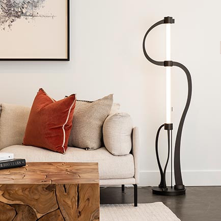 Beige sofa with two pillows, featuring a carved wooden coffee table and an artistic floor lamp.