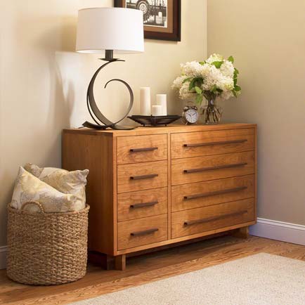 A dresser in a room with a lamp and a basket.