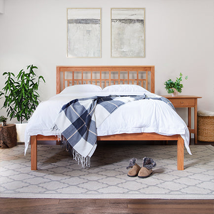 Wooden bed with checkered throw blanket and matching bedside table.