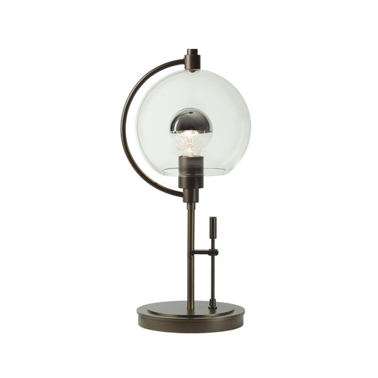 Hubbardton Forge Pluto Table Lamp featuring a round glass shade, sturdy metal base, and elegantly curved arm, handcrafted in Vermont.
