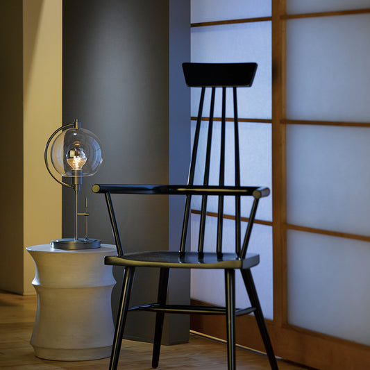 Black chair showcasing sleek design paired with Hubbardton Forge Pluto Table Lamp on chic white table.