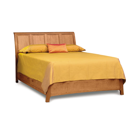 Copeland Furniture Sarah Sleigh Storage Bed in natural cherry wood with a headboard and built-in storage drawers, neatly made with a yellow bedspread and three pillows.