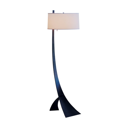 Stasis Floor Lamp by Hubbardton Forge featuring a sleek hand-crafted curved black metal stand paired with a classic white cylindrical shade.